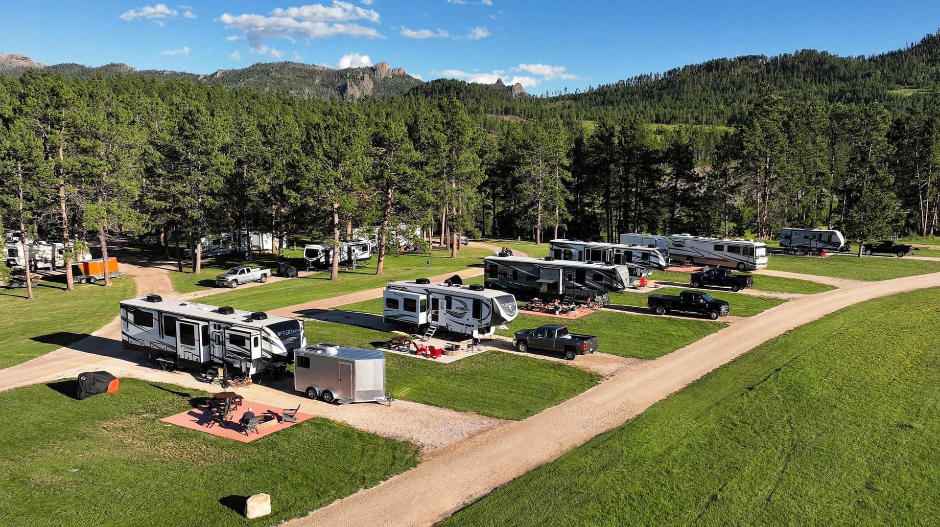 Aerial view of an RV park with several parked RVs and trucks surrounded by trees.
